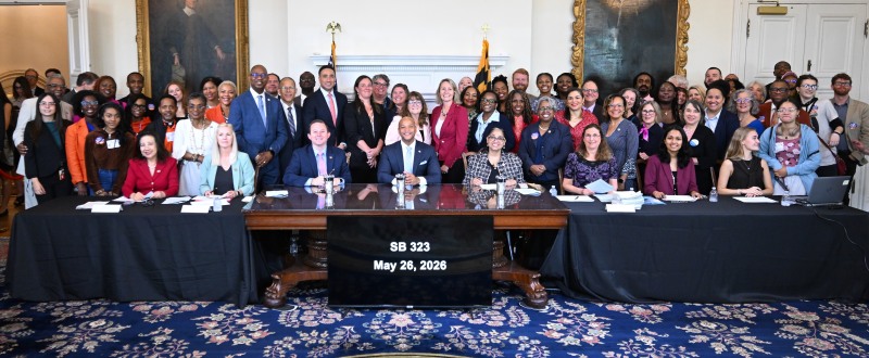 Maryland Governor Moore signing SB 323 surrounded by dozens of people