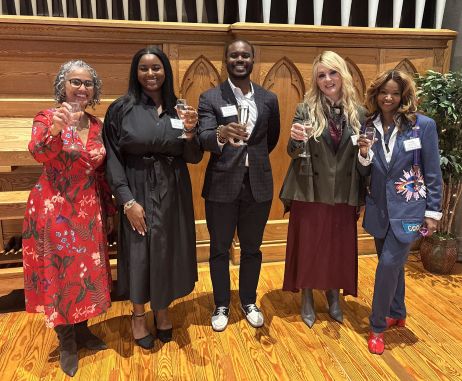 Five people standing on a stage hold up glasses in a toast