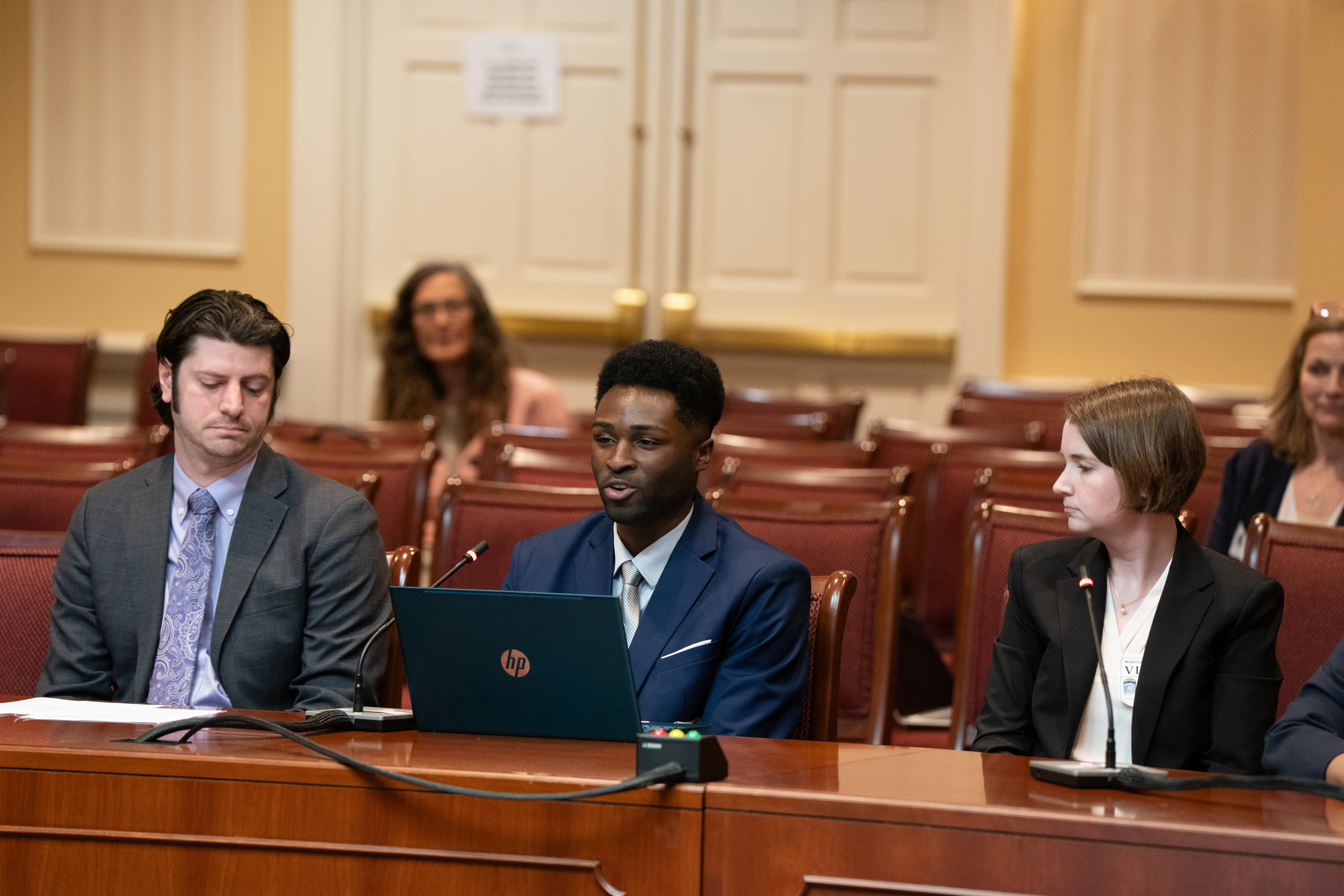 3 students in business attire seated in a row with a mic
