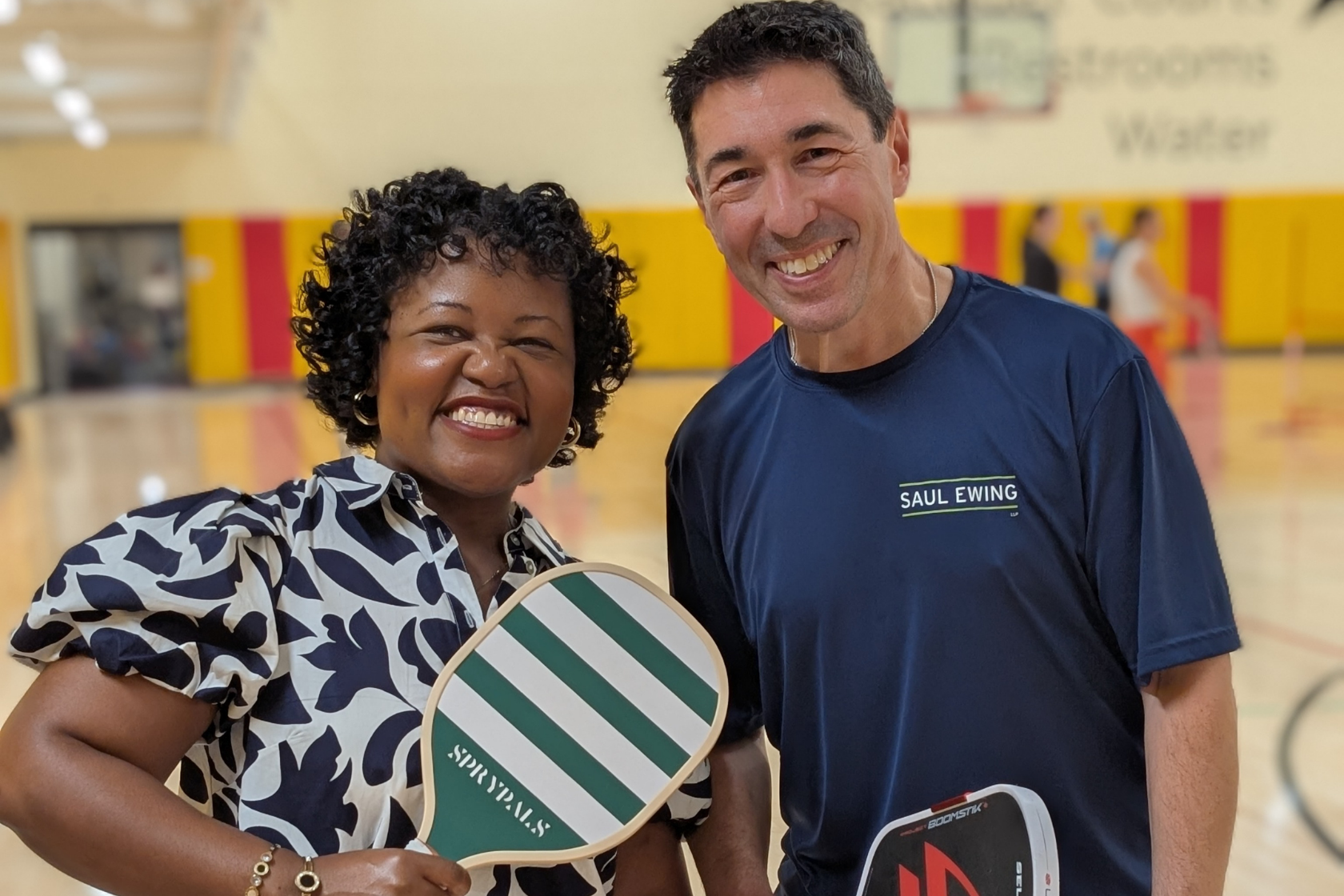 2 people in athletic clothing pose in a pickleball court holding rackets.