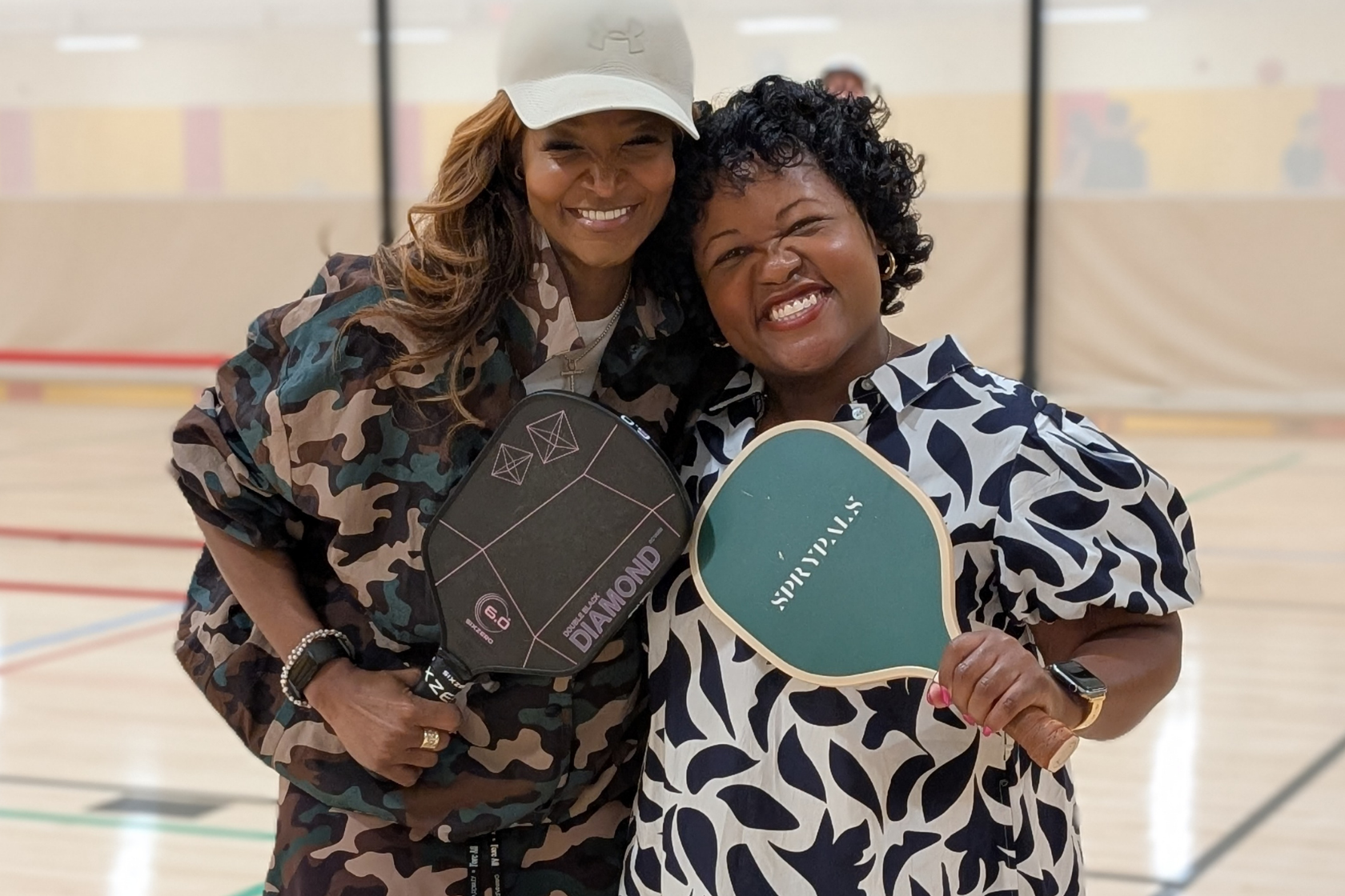 Two people smiling holding racquets on a pickleball court
